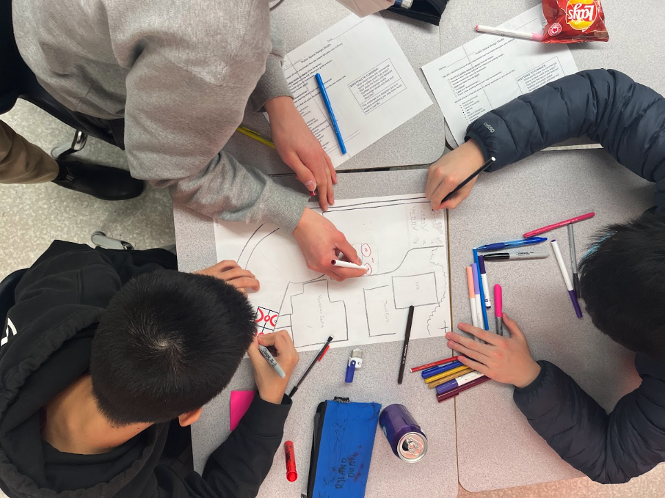 A photo from above that shows three students drawing a map of their school grounds. 